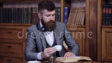 优雅的男人喝茶，在图书馆看书。 一个人喜欢读一本书。 穿着豪华西装的胡子男